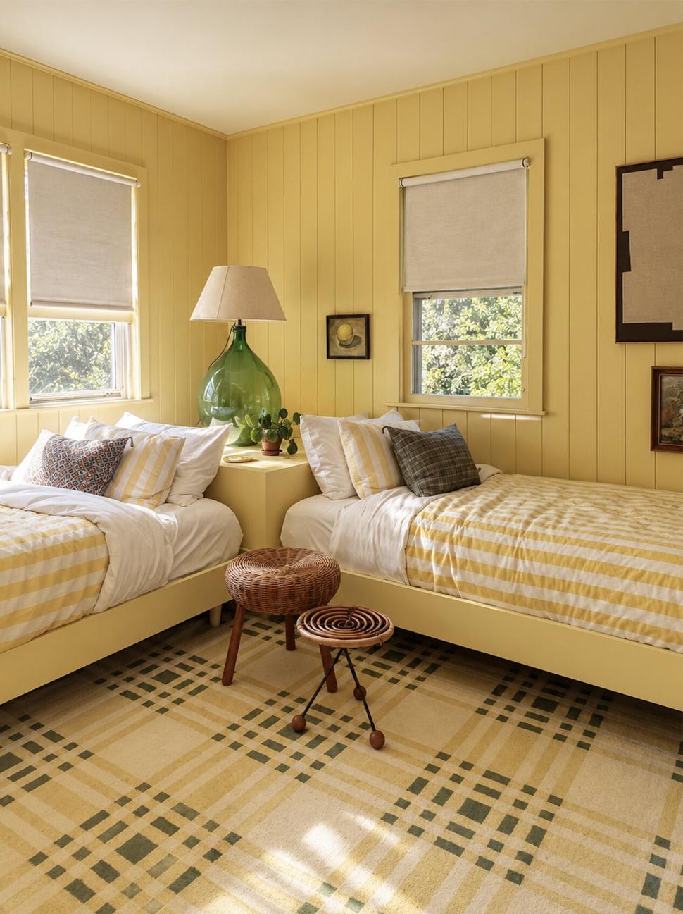 Ranch & Barn — yellow-panelled twin bedroom with striped quilts, a green glass lamp, a woven stool and a plaid rug