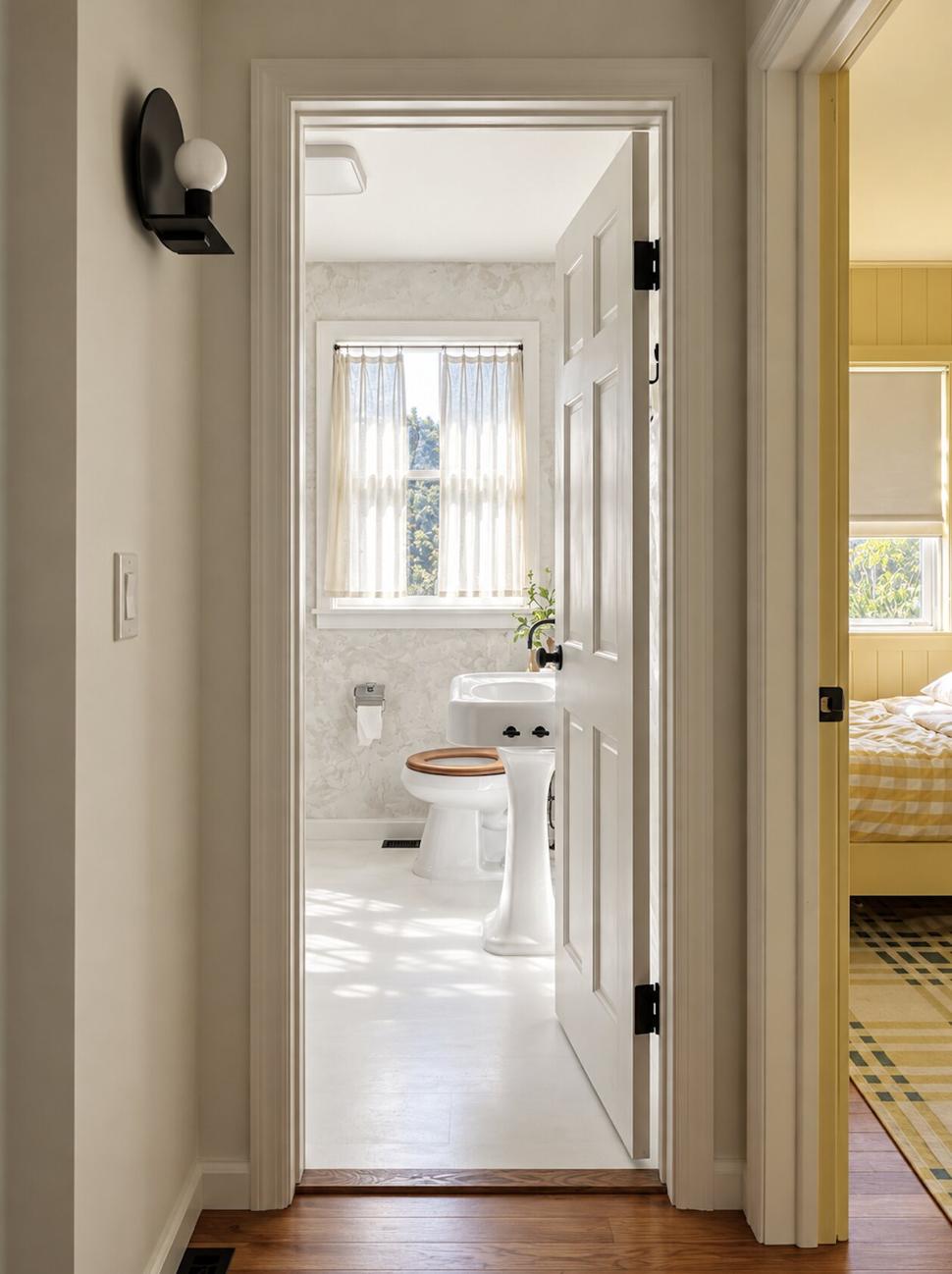 Ranch & Barn — hallway view through to the bath, with a black globe sconce, a pedestal sink and a wood-seat toilet