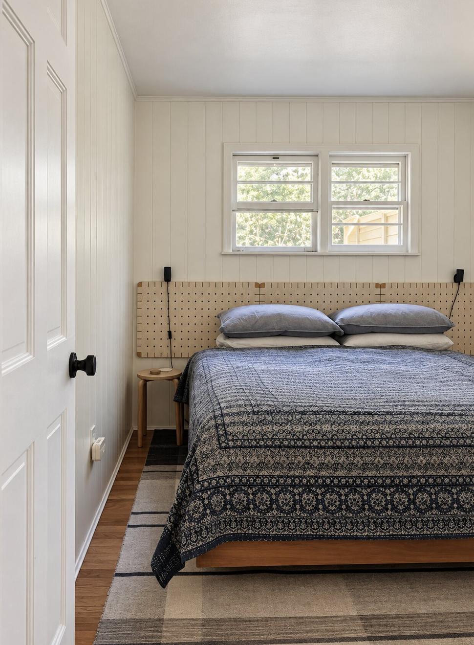 Ranch & Barn — bedroom with a woven-strap headboard, an indigo block-printed coverlet and a plaid rug beneath a double window